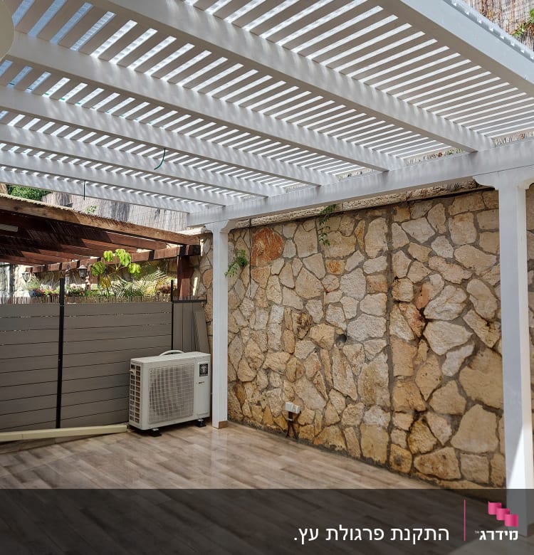 פרגולה לבנה מעל רצפת דק ליד קיר אבן